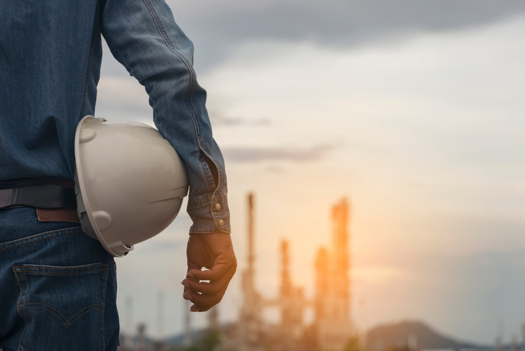 Engineer and safety Officer concept. Young man engineer holding white safety hat (helmet).Construction Safety Officer  inspector in front of refinery plant back